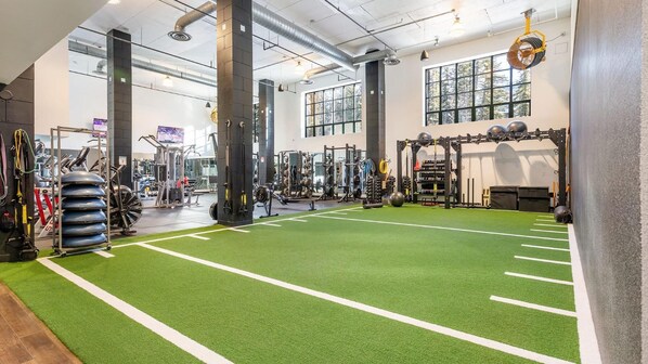 Ein Fitnessstudio mit grünem Rasenbelag, Gewichte und großen Fenstern.