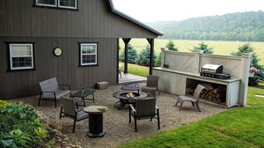 Eine überdachte Terrasse im Freien mit Sitzgelegenheiten, einem Feuerkorb und einem Grill.