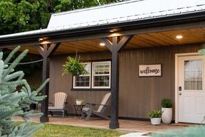A covered porch with two chairs, a welcome sign, and potted plants.