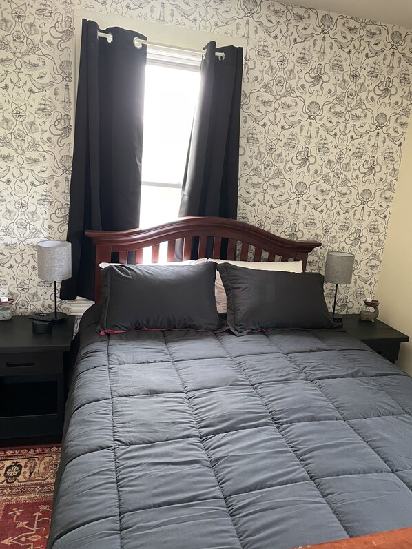 Un dormitorio con cabecera de madera, colcha acolchada gris, dos lámparas de noche y un papel tapiz estampado.