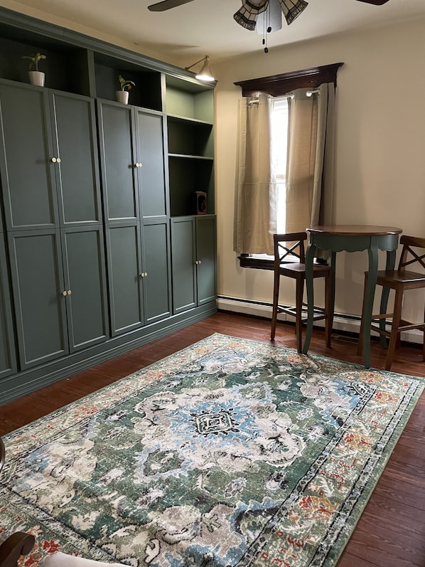 A room with a large green cabinet, a wooden table with two chairs, a patterned rug, and a window with curtains. - Cutlass Private Room close to LBI Long Beach Island West Creek Tuckerton Wedding (Eagleswood)
