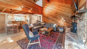 Un salon chaleureux de style loft, doté d’une cheminée en pierre, de poutres apparentes en bois et d’un coin repas avec une grande table et des chaises.