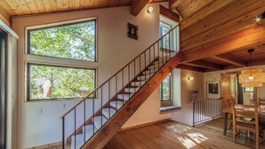 Une pièce spacieuse avec un escalier en bois, de grandes fenêtres et un coin repas.