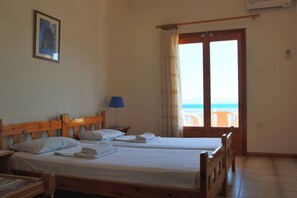 A room with two wooden beds, a framed picture on the wall, a lamp, and a view of the sea through a door.