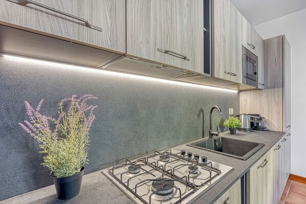 Een moderne keuken met een gasfornuis, een zwart aanrecht en houten kastjes.