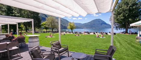 An outdoor seating area with tables and chairs, overlooking a lake and mountains.