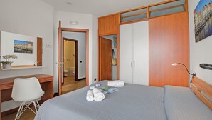 Een hotelkamer met een bed, een bureau, een stoel, een kledingkast en een schilderij aan de muur.