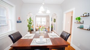 Een eetkamer met een houten tafel gedekt voor vier personen, witte wanden en uitzicht op de woonkamer.