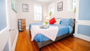 Een slaapkamer met een bed, een dressoir, een raam en een deur.
