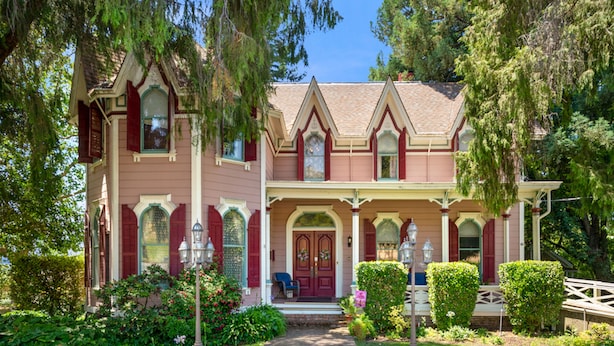 A two-story house with a front porch, a red door, and a garden with various plants and a pathway leading to the entrance. - The Gables Wine Country Inn (Santa Rosa)