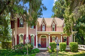 A two-story house with a front porch, a red door, and a garden with various plants and a pathway leading to the entrance.