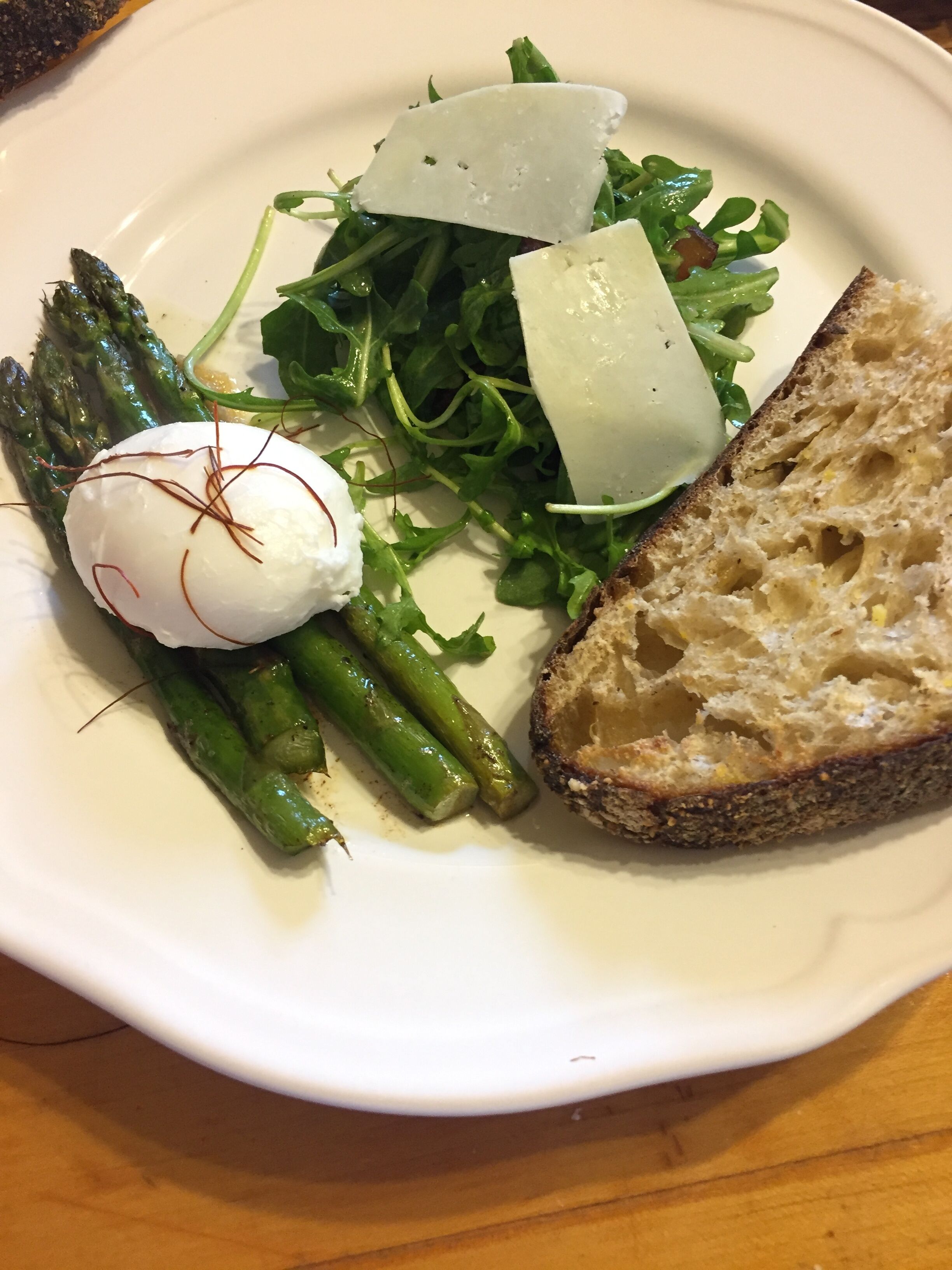 Un plato con un huevo pochado, espárragos, rúcula y una rebanada de pan.