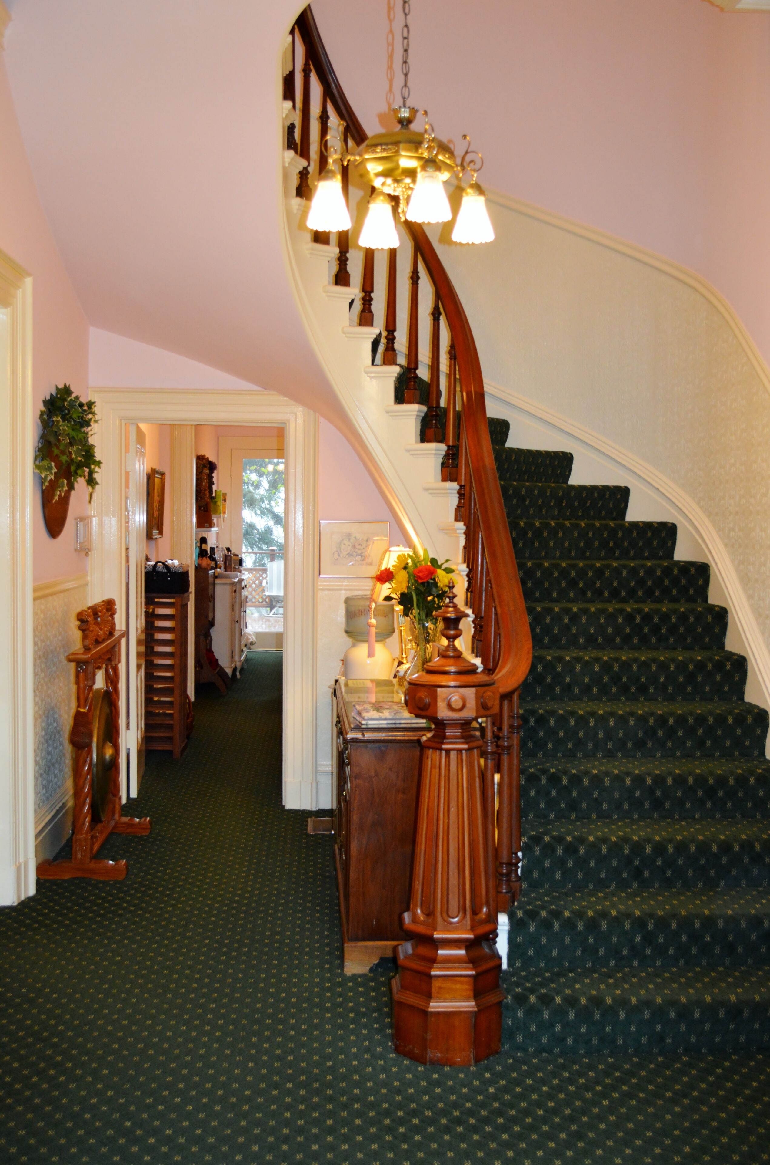 Una imponente escalera con barandilla de madera y un candelabro, que conduce a un rellano con un jarrón de flores.