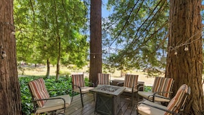 A deck with four striped chairs and a square table, surrounded by large trees and a sandy area. - The Gables Wine Country Inn (Santa Rosa)