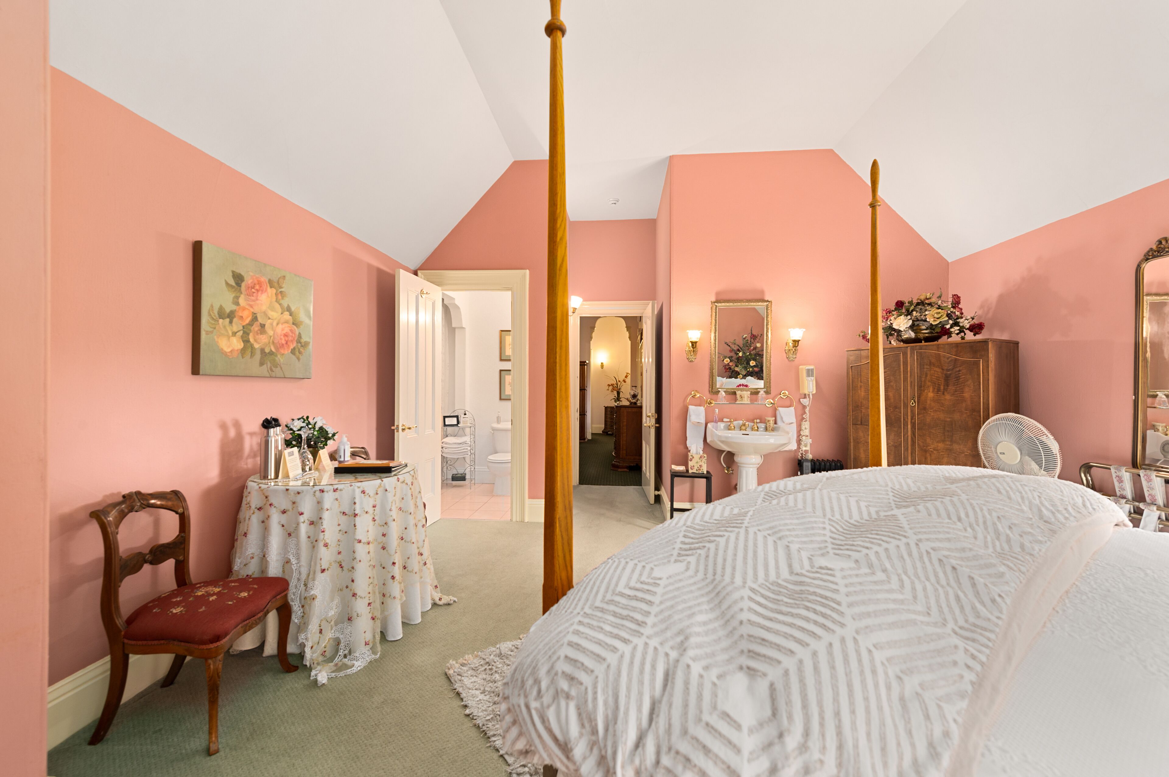 A bedroom with a four-poster bed, a vanity with a mirror, and a chair.