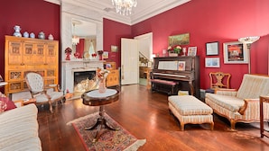A room with a red wall, a piano, a chandelier, and a wooden cabinet. - The Gables Wine Country Inn (Santa Rosa)