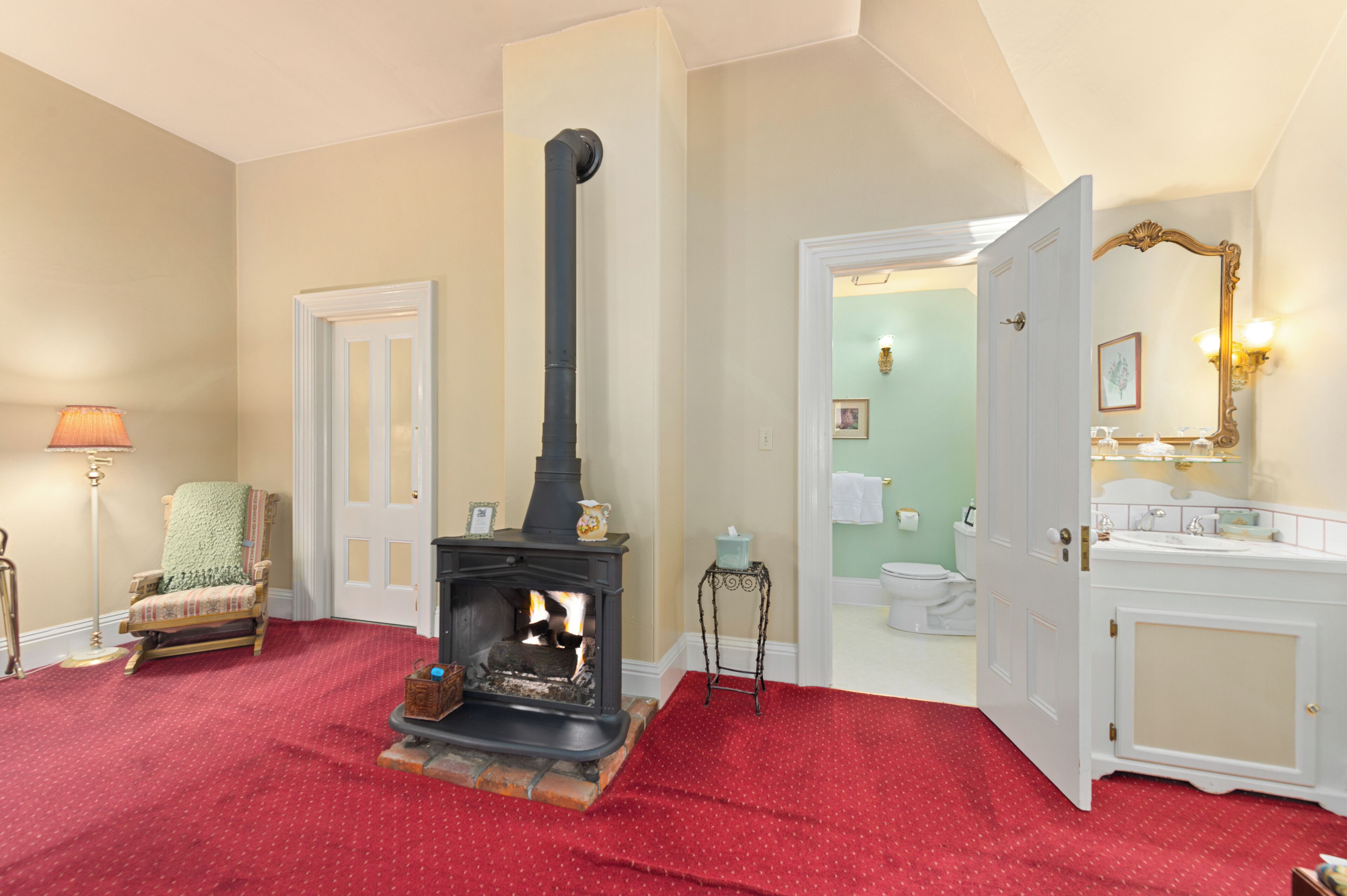 A room with a fireplace, a chair, a small table, and a bathroom visible through an open door.