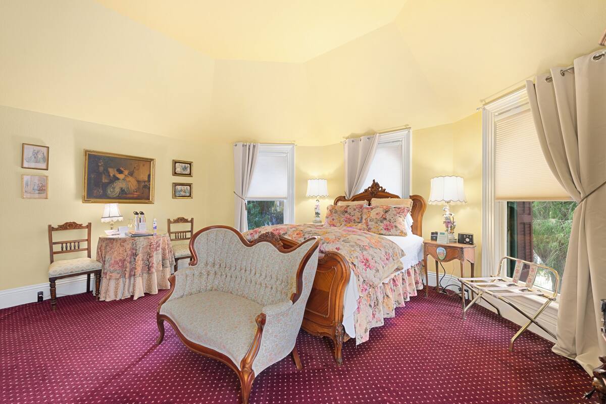 A bedroom with a large bed, a chair, a bedside table, and a window with curtains.