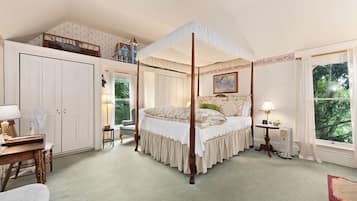 Una cama con dosel y cortinas, un edredón floral, un escritorio con lámpara y vista a una casa azul a través de una ventana.