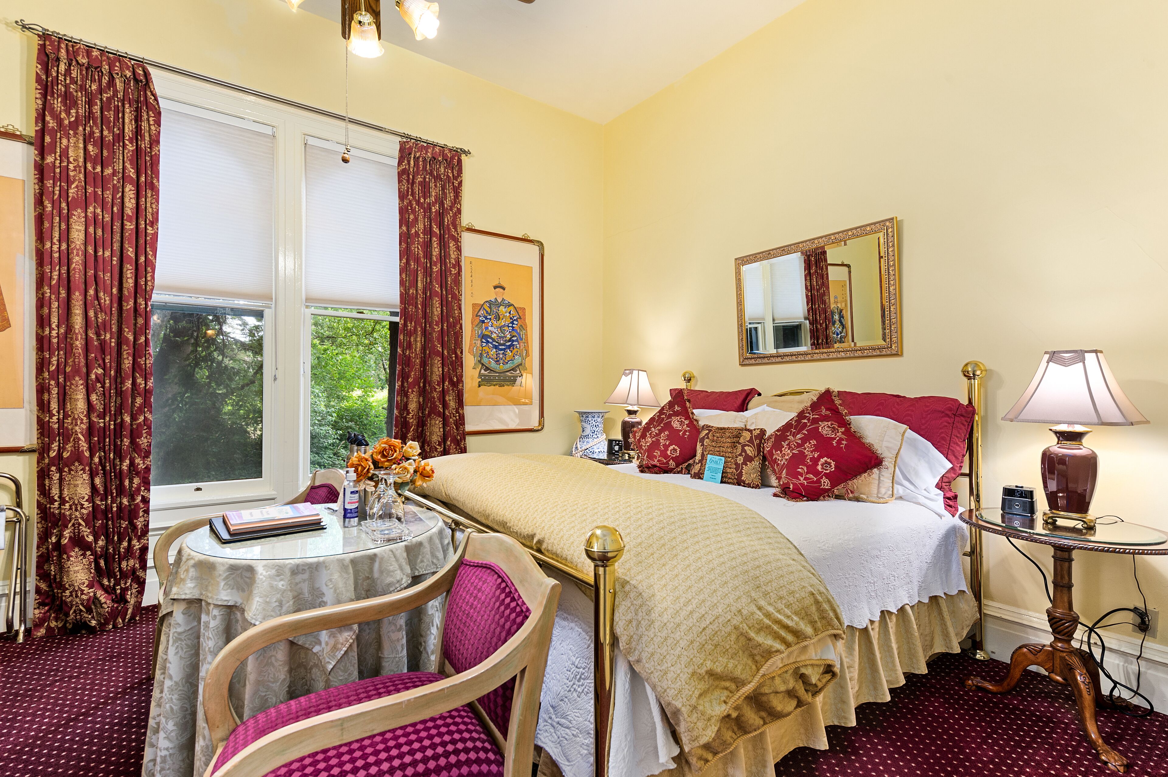 Une chambre d’hôtel avec un lit, une table ronde entourée de chaises, une petite table avec une lampe et une fenêtre avec des rideaux.