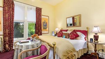 Une chambre d’hôtel avec un lit, une table ronde entourée de chaises, une petite table avec une lampe et une fenêtre avec des rideaux.