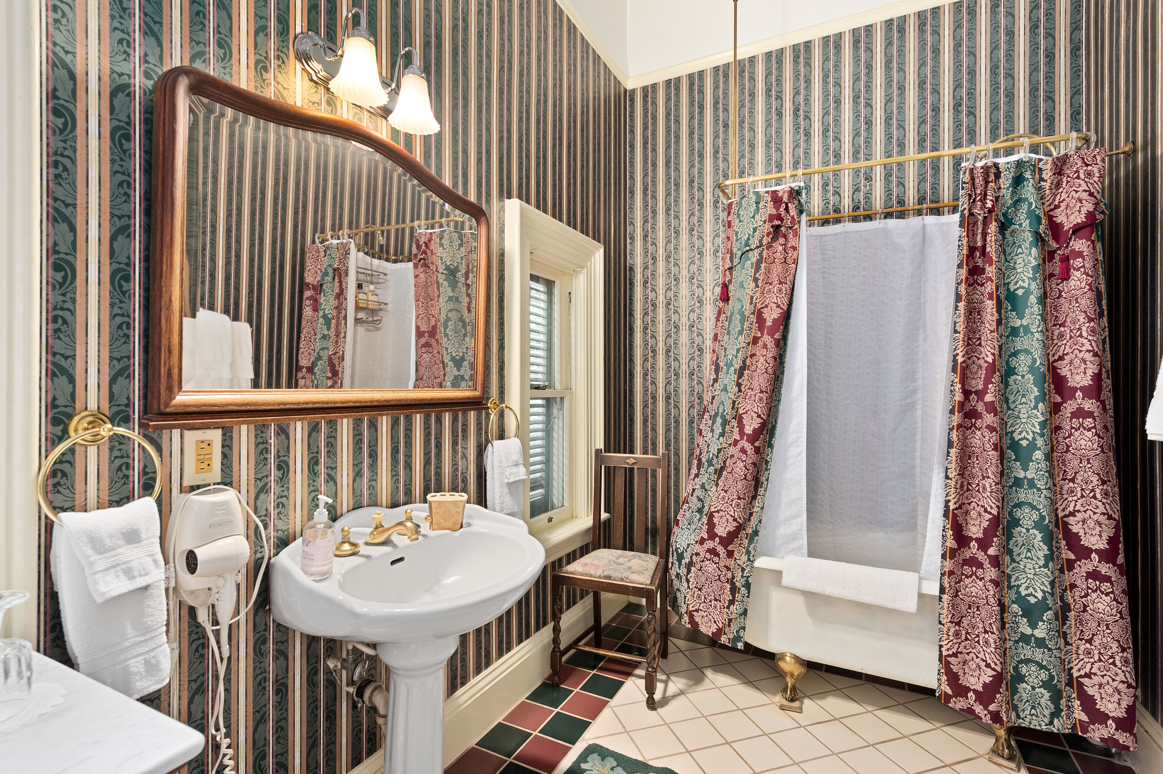 A bathroom with a large mirror, a sink, a chair, and a bathtub.