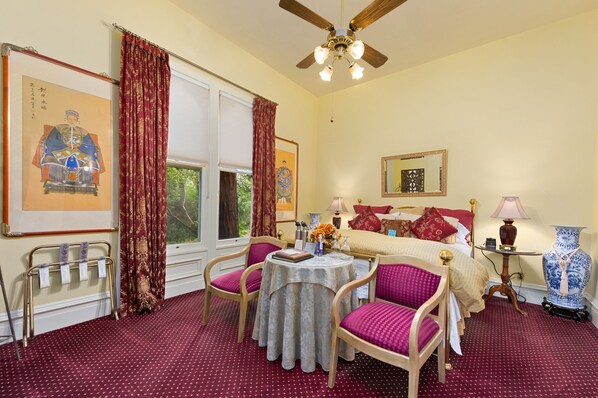 A traditional room with a bed, a round table with chairs, a ceiling fan, and a large vase.