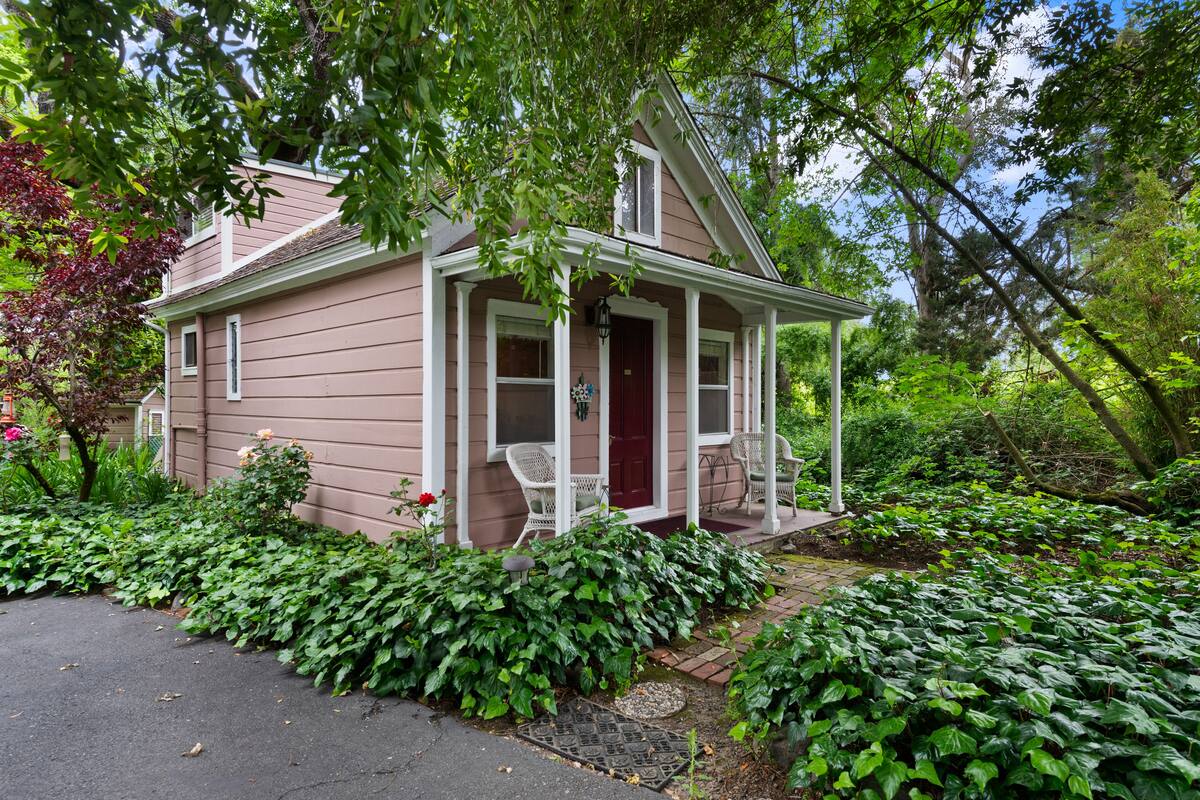 A single-story house with a porch, surrounded by lush greenery and a garden.