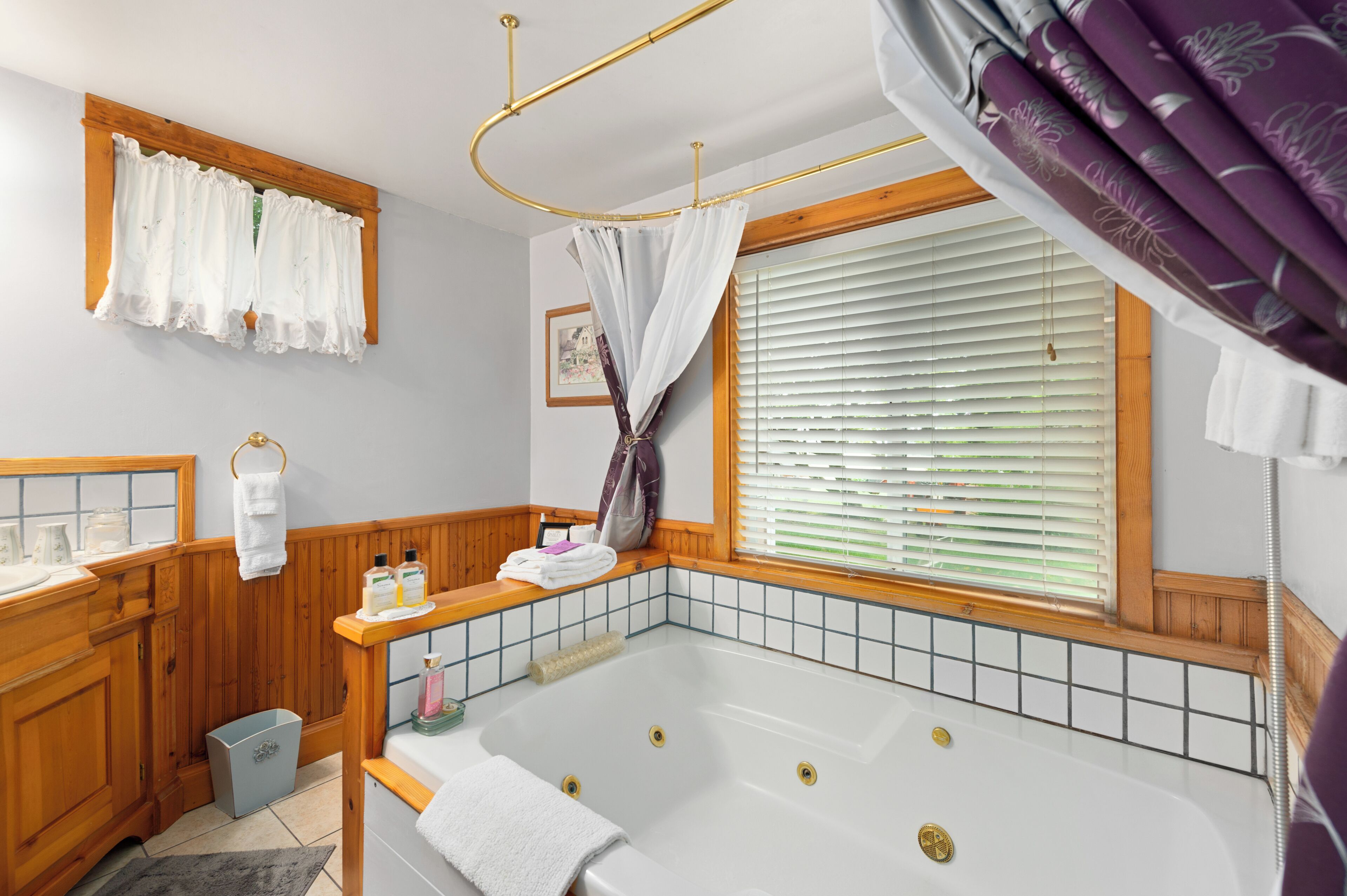 Ein Badezimmer mit einer Badewanne, Holzschränken, einem Waschtisch und einem Fenster mit Jalousien und Vorhang.