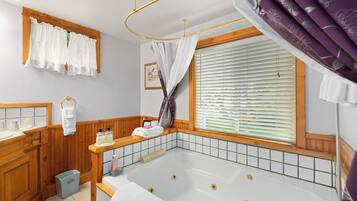 Ein Badezimmer mit einer Badewanne, Holzschränken, einem Waschtisch und einem Fenster mit Jalousien und Vorhang.