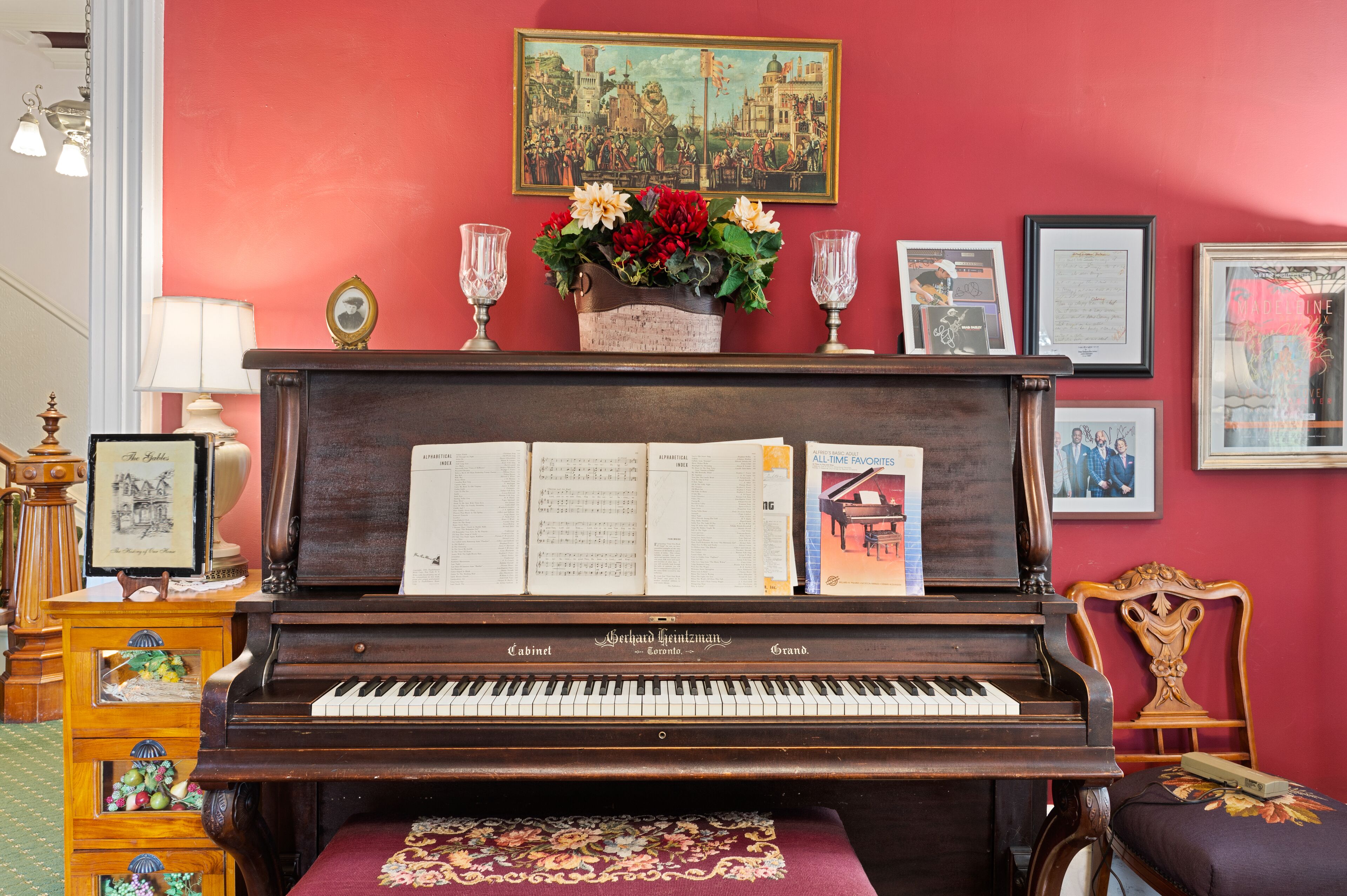 A grand piano with sheet music, a framed painting, and decorative items on a mantelpiece.