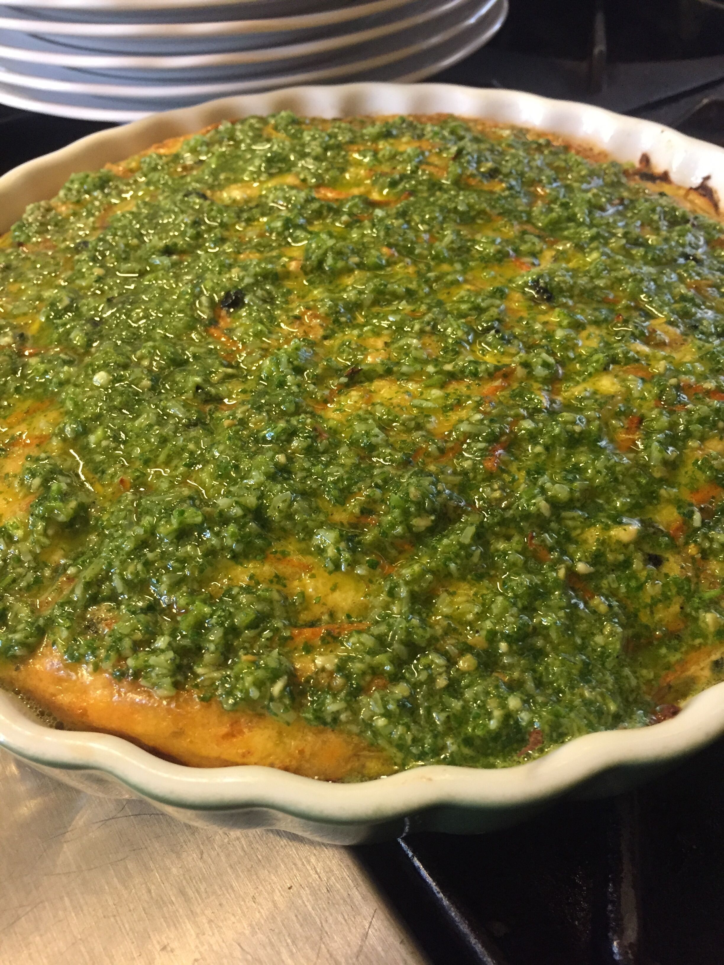A round dish with a green topping, placed on a stove.