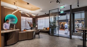A modern reception area with a curved desk, seating, and a glass wall leading to a shop.
