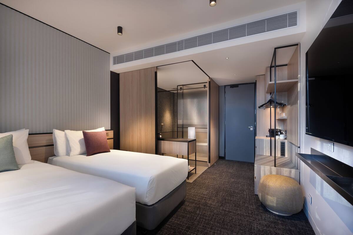 Una habitación de hotel moderna con dos camas, televisión, minibar y vestidor.