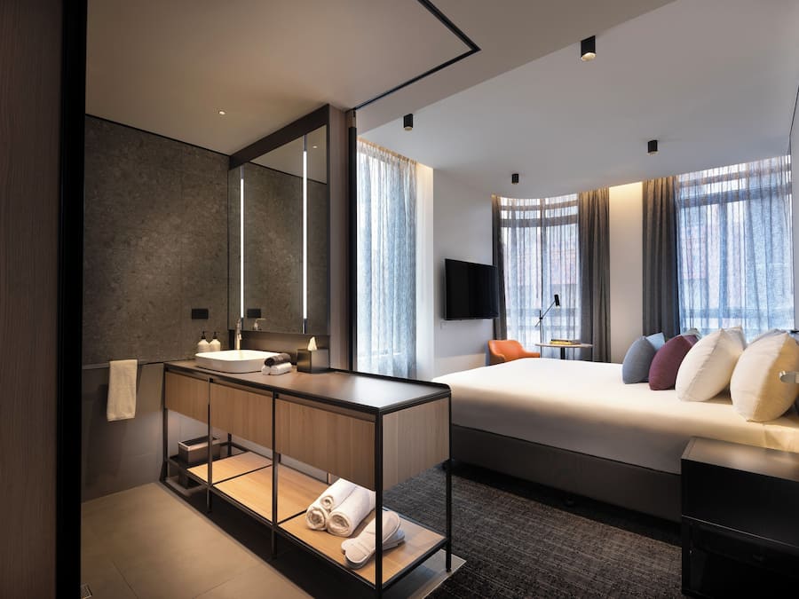 Camera d'albergo moderna con un ampio letto, un comodino, una TV integrata e un grande specchio.