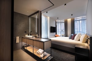 Quarto de hotel moderno com uma cama grande, uma mesinha de cabeceira, televisão integrada e um espelho amplo.