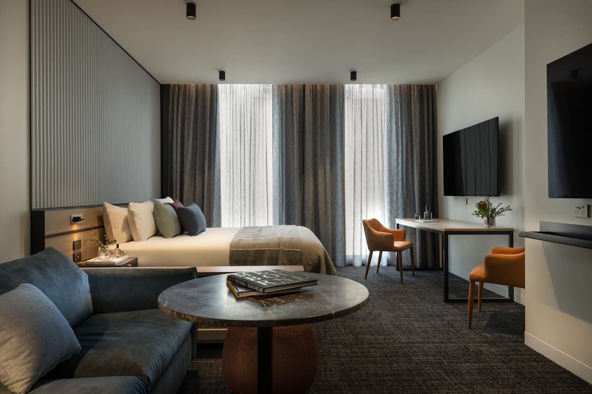 Una habitación de hotel moderna con una cama, un sofá, un escritorio y un televisor.