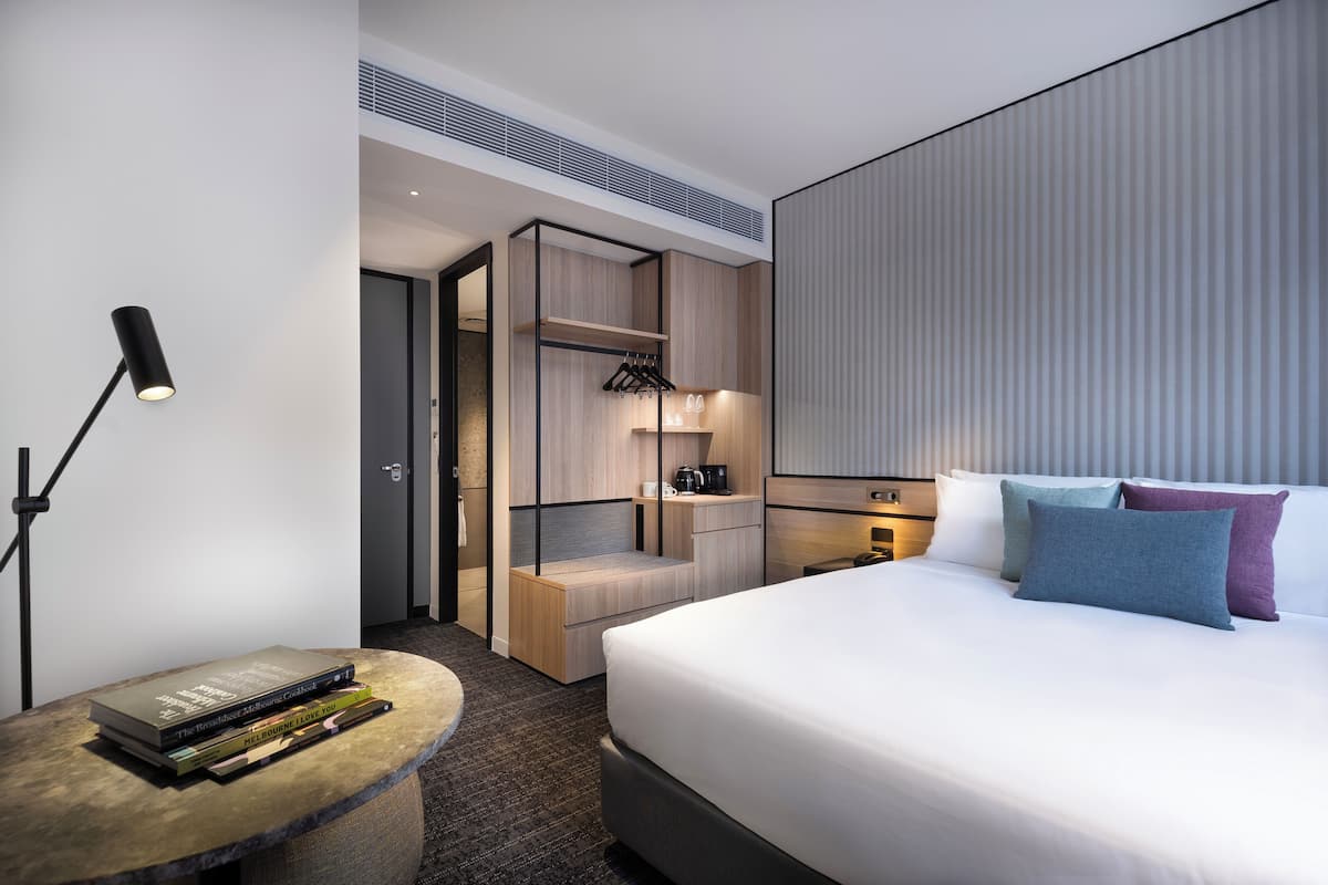 Una habitación de hotel moderna con una cama grande, mesitas de noche, un área de estar y una kitchenette.