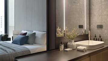 A modern hotel room with a large bed, a bedside table with a vase of flowers, a white sink, and a large mirror.