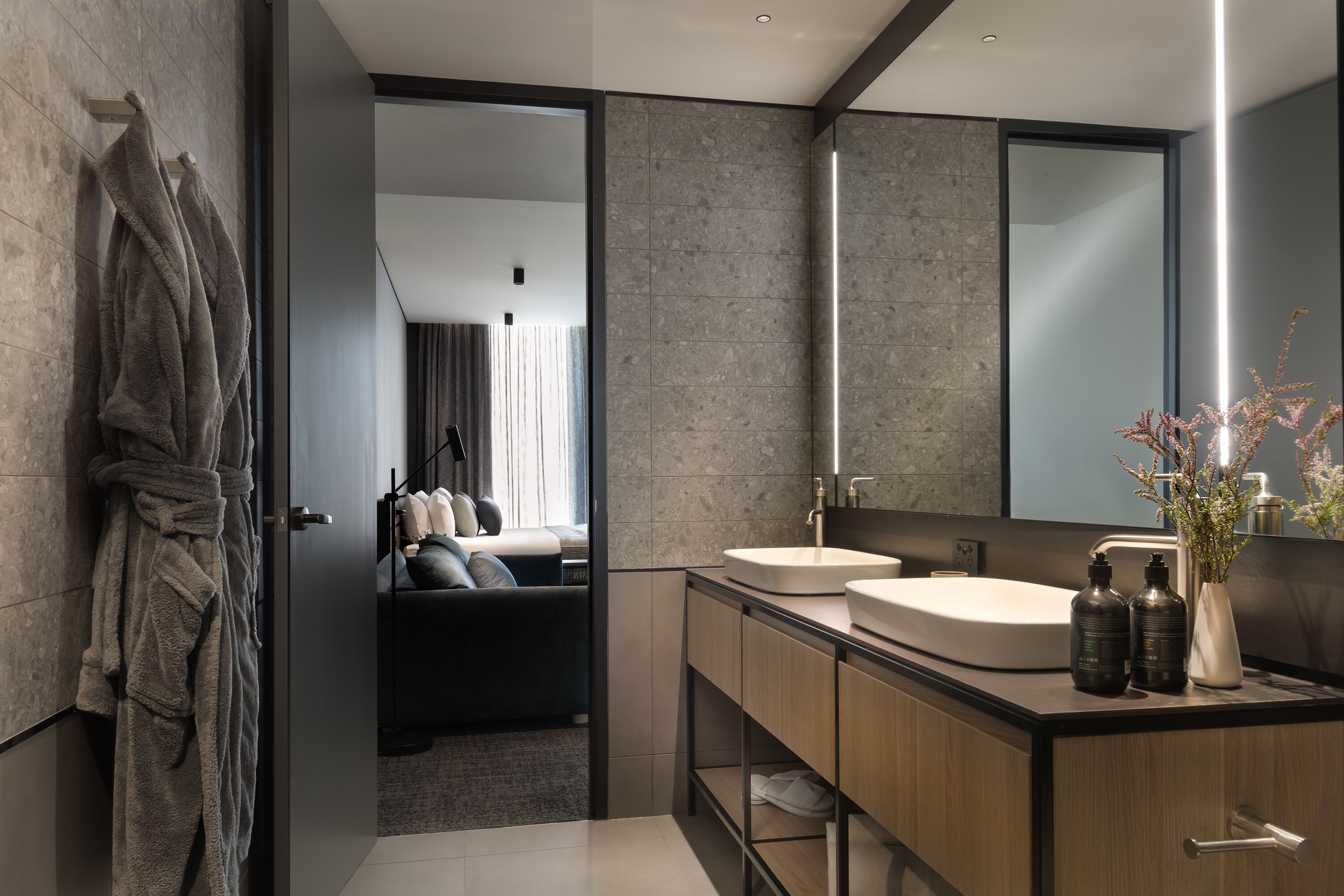 A modern bathroom with a large mirror, two sinks, and a robe hanging on the wall.