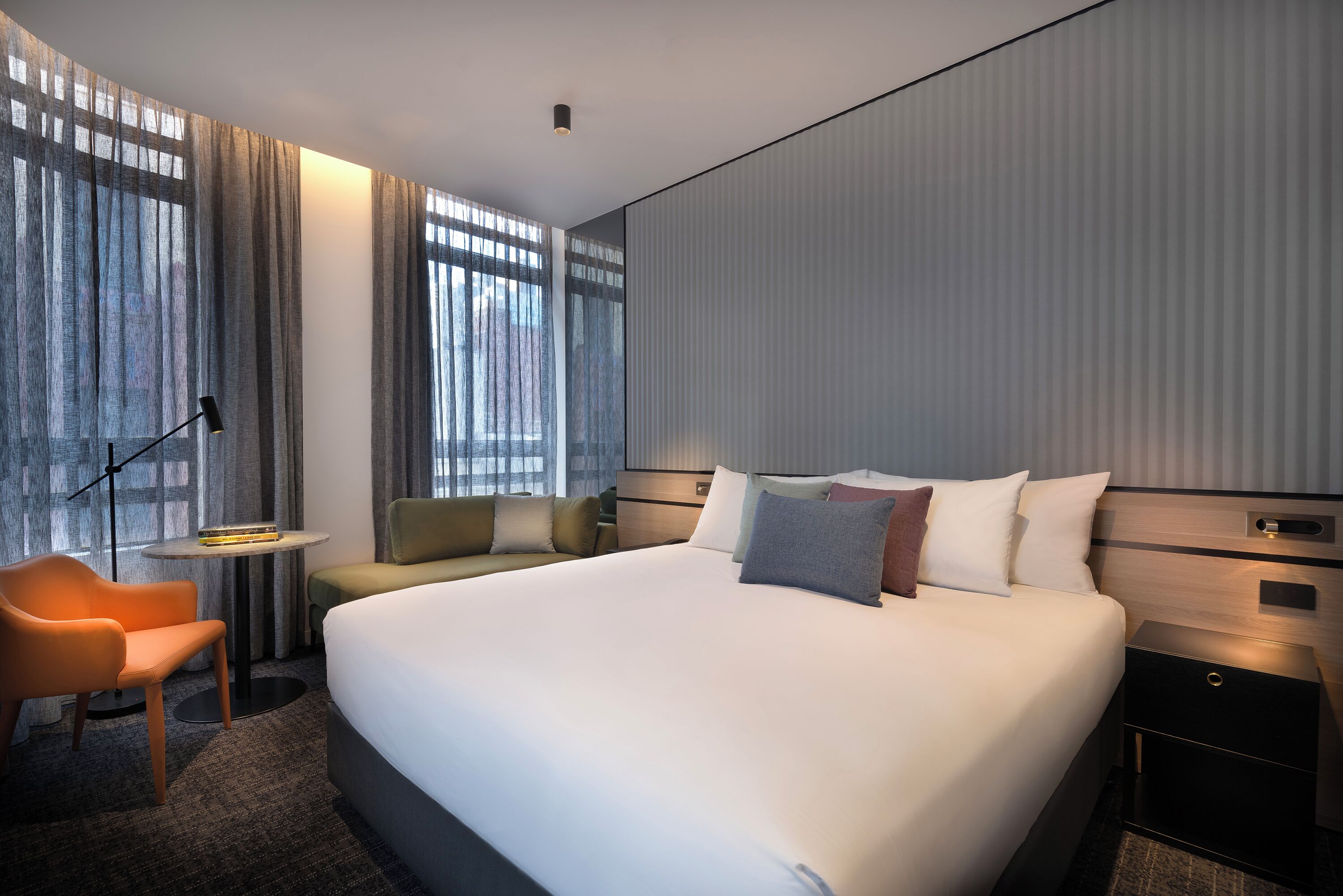 A modern hotel room with a large bed, a sofa, a desk, and a chair.