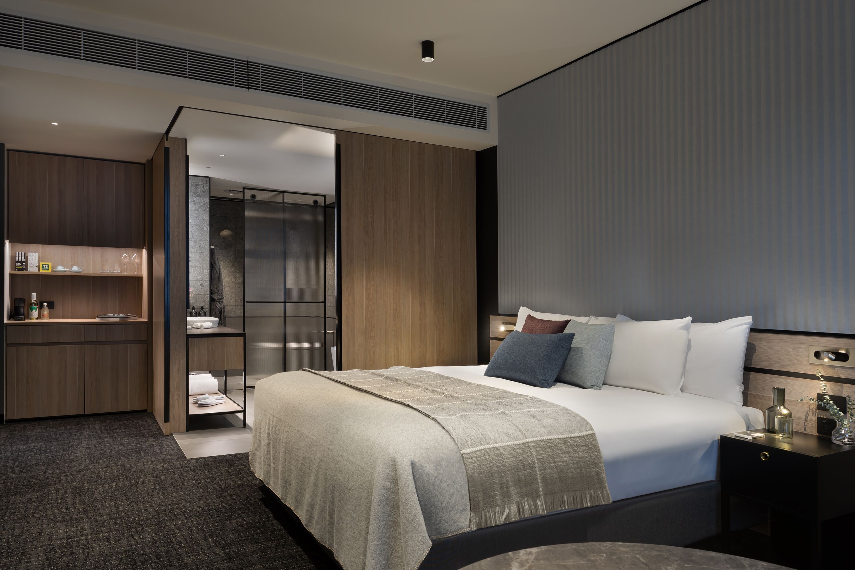 Une chambre d’hôtel moderne dotée d’un grand lit, d’une armoire intégrée, d’une petite kitchenette et d’une porte-fenêtre coulissante donnant sur la salle de bain.
