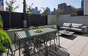 Un patio en la azotea con una mesa, sillas, un sofá y una pequeña maceta.