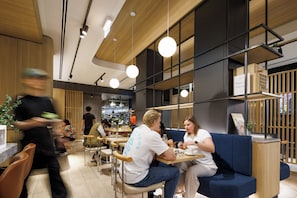 A modern cafe interior with wooden accents, round pendant lighting, and a visible kitchen area. - The Howey (Melbourne)
