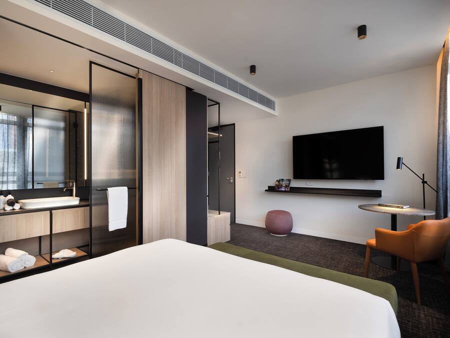 Ein modernes Hotelzimmer mit einem großen Bett, einem Einbauschrank, einem Flachbildfernseher, einem kleinen runden Tisch und einem Stuhl.