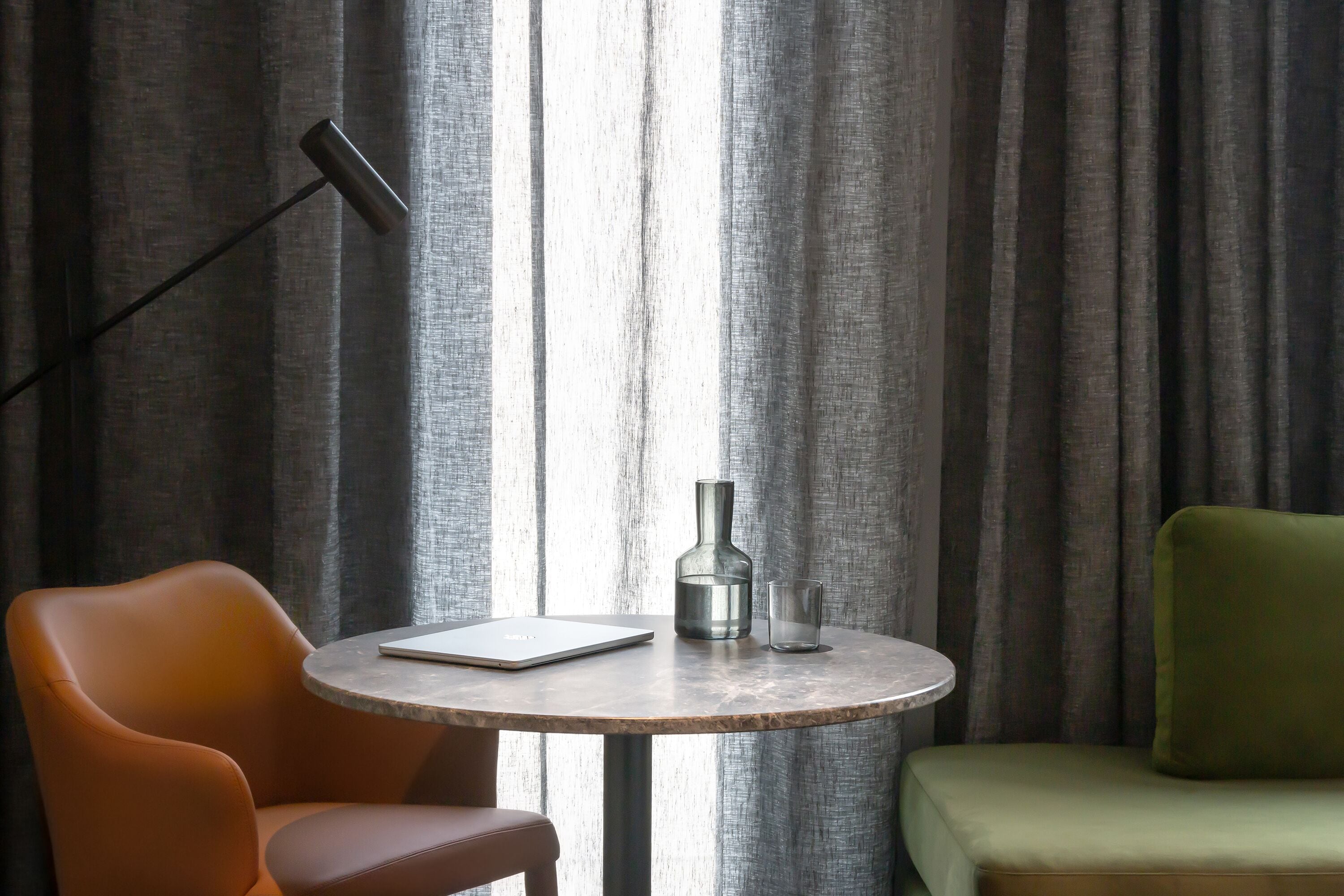 A room with a round table, a laptop, a bottle, and a glass.