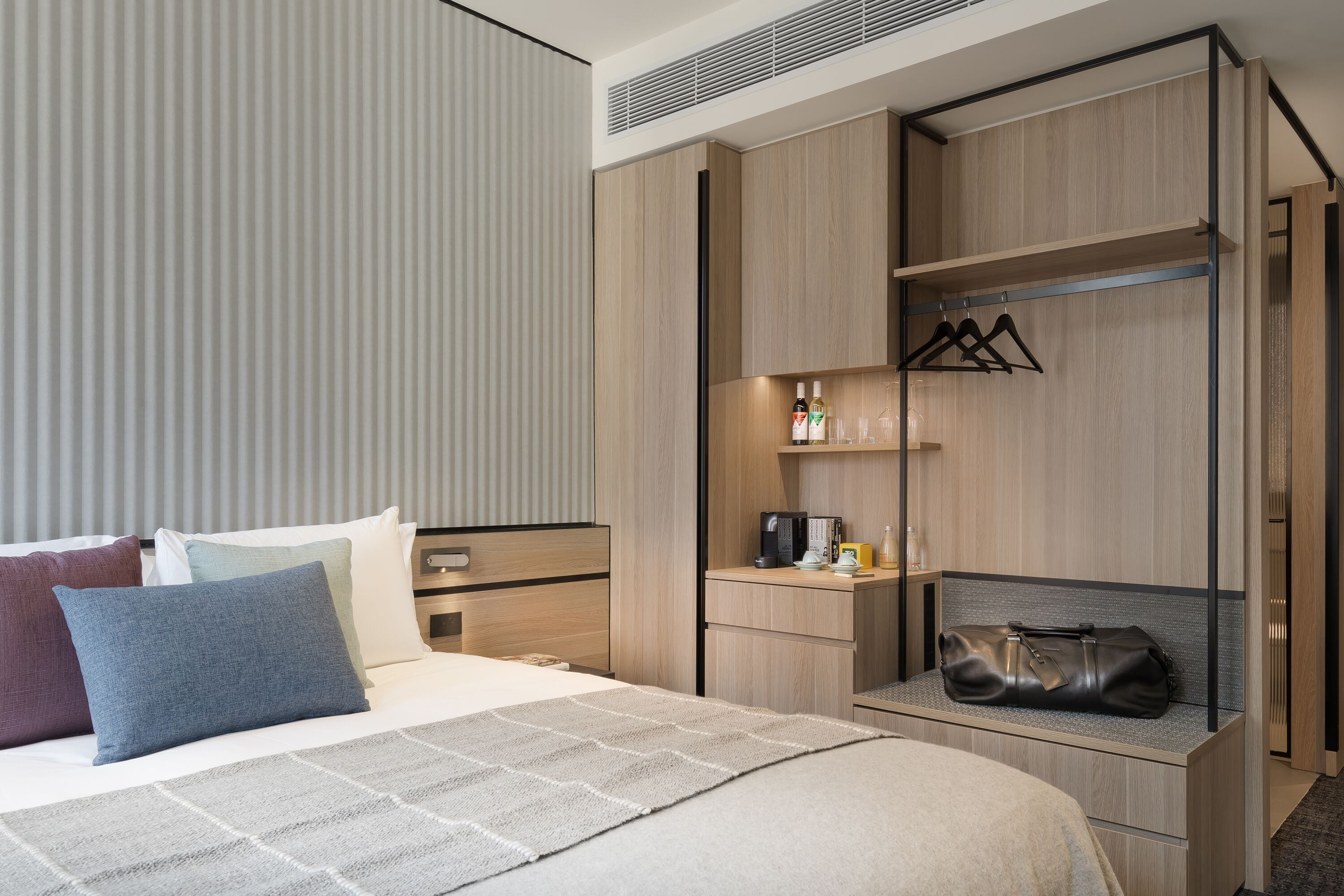 A hotel room with a bed, a desk, a wardrobe, and a shelf with toiletries.