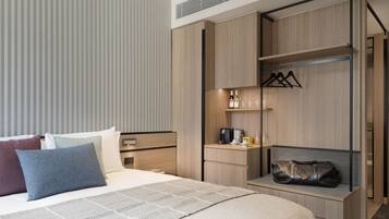 A hotel room with a bed, a desk, a wardrobe, and a shelf with toiletries.