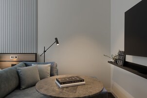 Una sala de estar moderna con un sofá gris, una mesa redonda para café con libros, una lámpara de pie y un estante negro con objetos decorativos.