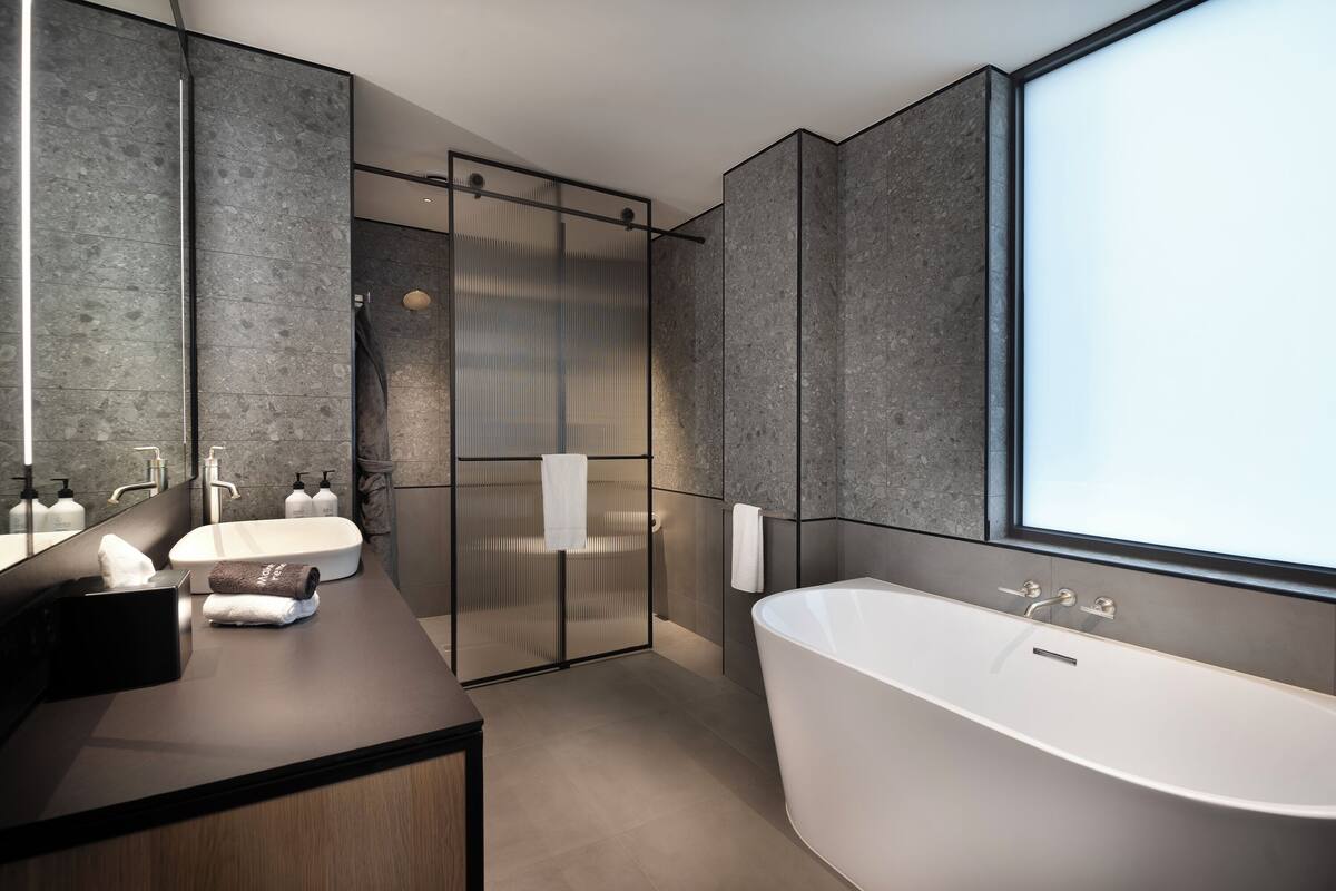 Un baño moderno con una bañera independiente, una ducha con mampara de vidrio y un tocador con espejo y toallero.